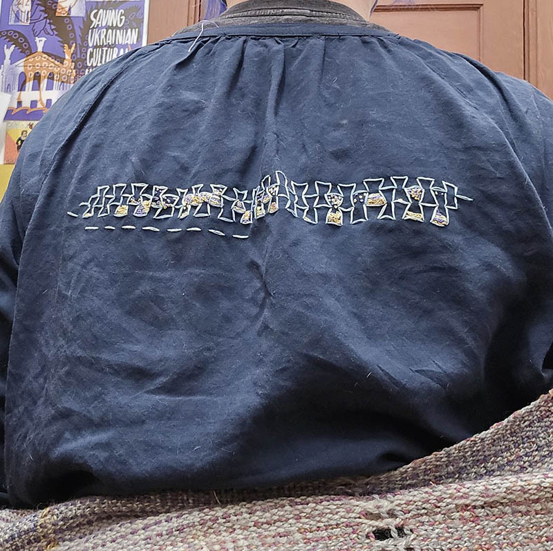 The back of a shirt, with rows of hourglass shapes filled with French knots and chain stitches in brown and purple