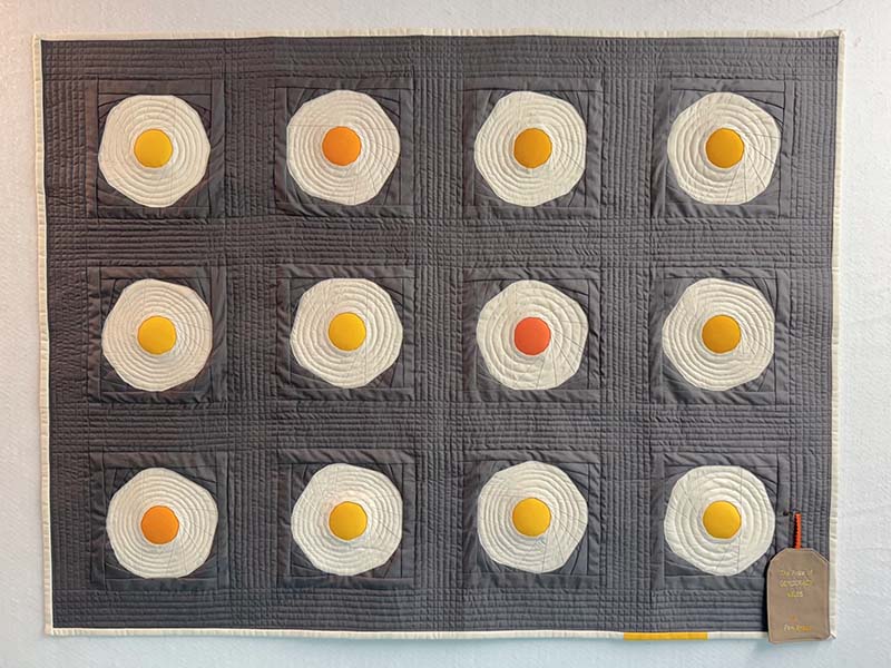 A quilt depicting a dozen eggs with an embroidered tag at the bottom